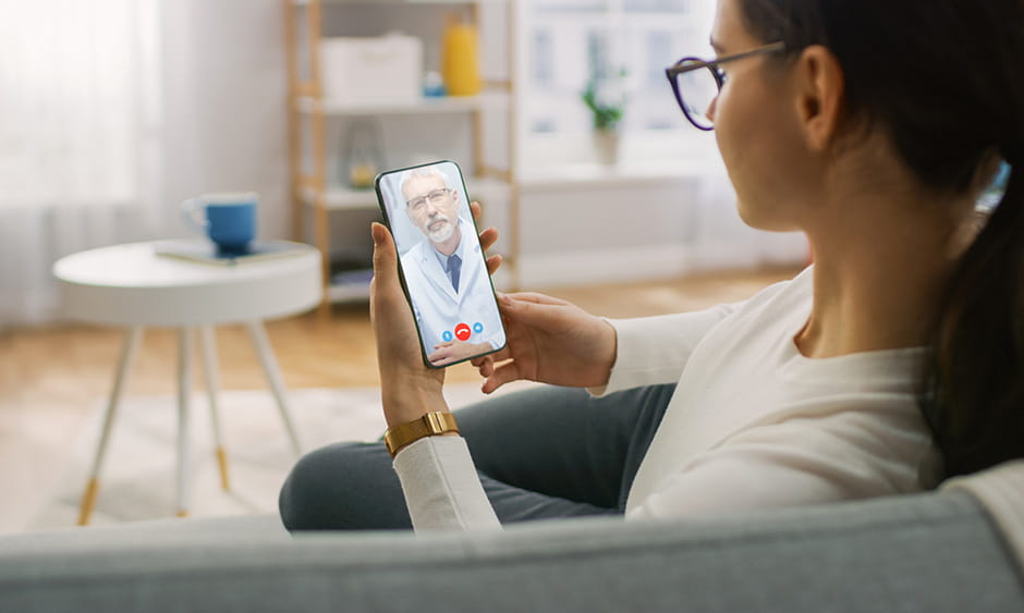 Woman sitting on couch at home using telehealth service on her phone